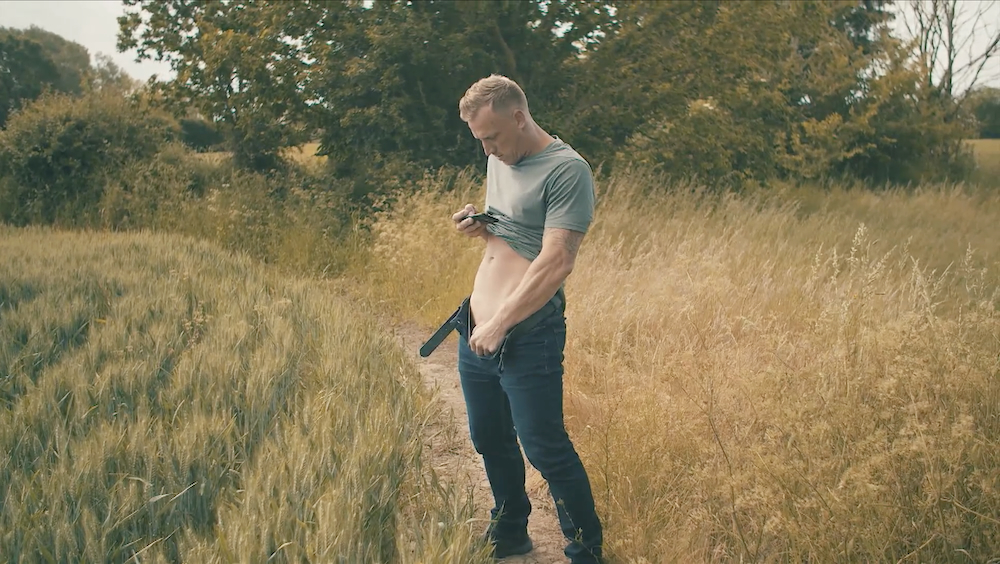 Luke Hardy takes a selfie of his hard cock, standing in field.